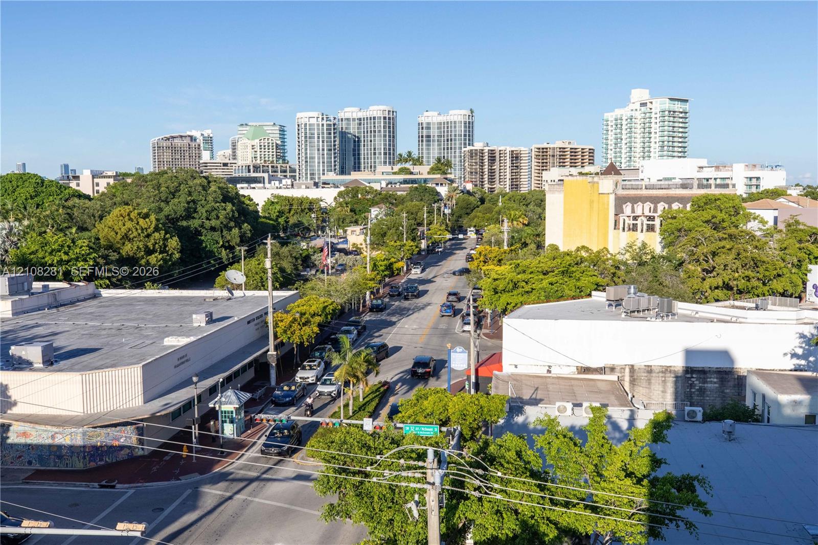 Aerial perspective showcasing urban surroundings featuring mature tree canopy, multi-story buildings, and city skyline
