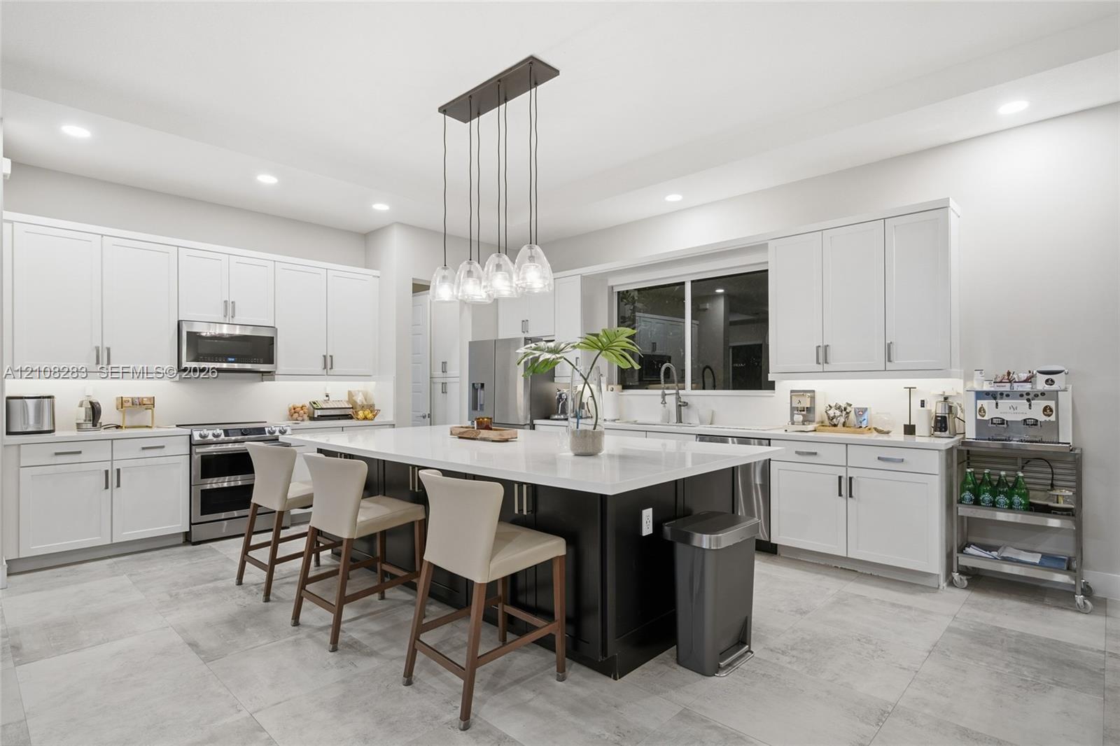 Kitchen featuring white Shaker-style cabinetry, a central island with a contrasting dark base and stone countertop, stainless steel appliances, recessed ceiling lighting, and tile flooring
