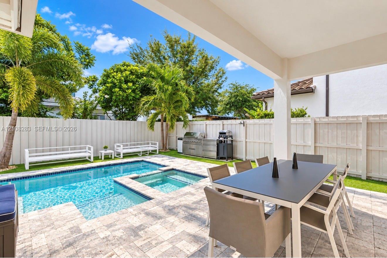 Covered patio featuring stone-tiled decking, a swimming pool with integrated spa, built-in stainless steel outdoor kitchen, and vinyl privacy fencing
