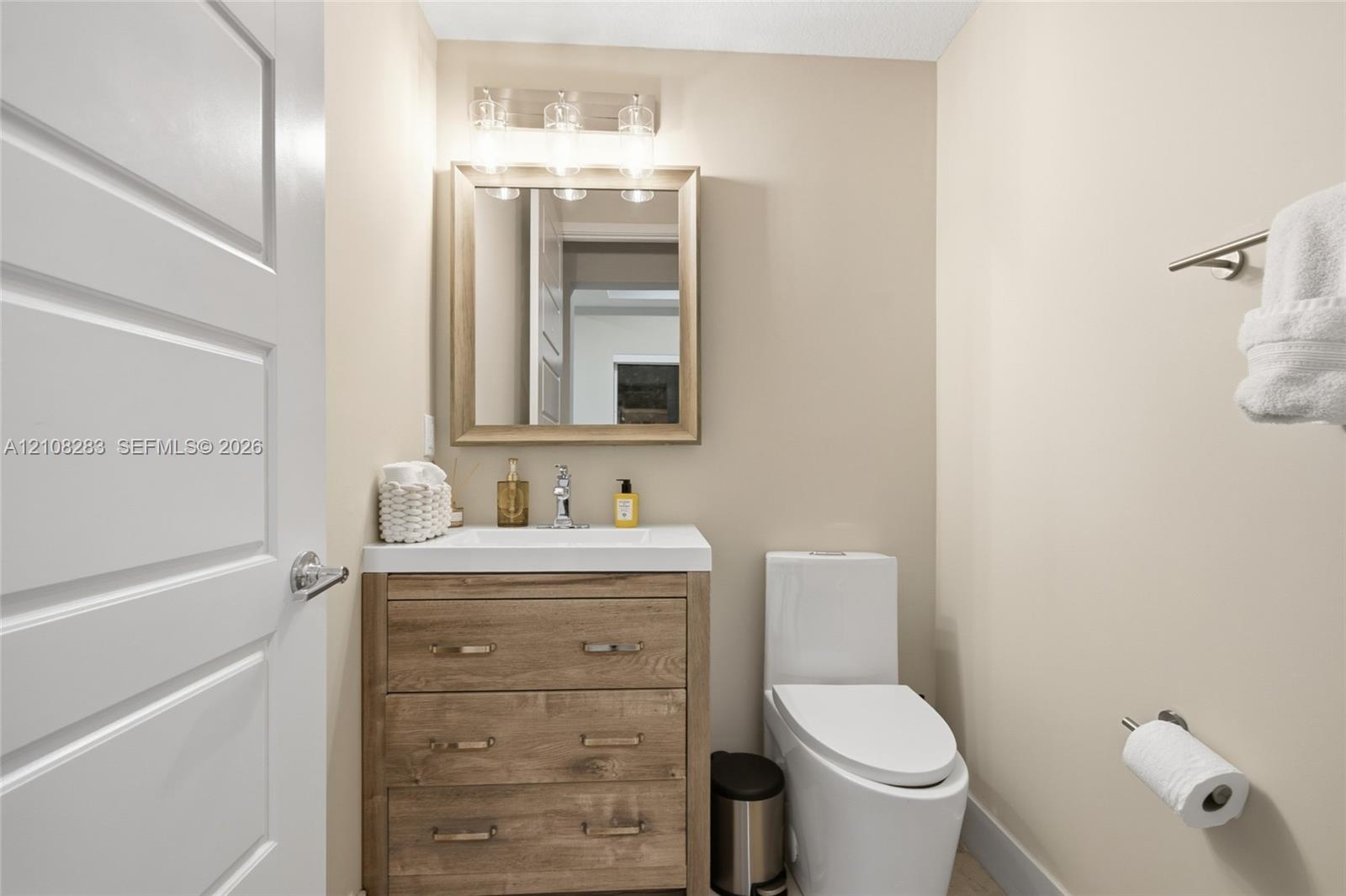 Bathroom featuring a wood-finish vanity with a rectangular sink, wall-mounted light fixture, framed mirror, and elongated dual-flush toilet
