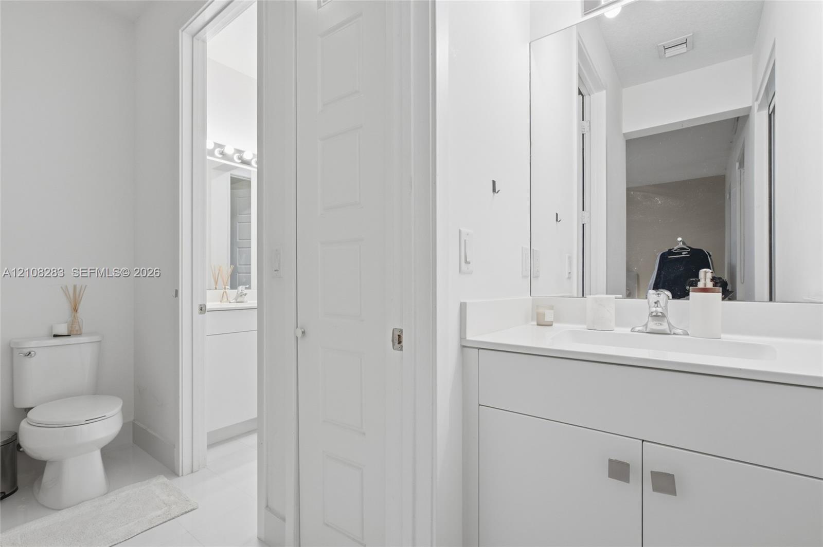 Bathroom featuring a white vanity cabinet with a stone-top integrated sink, a full-height wall mirror, a polished chrome faucet, and a standard-height toilet
