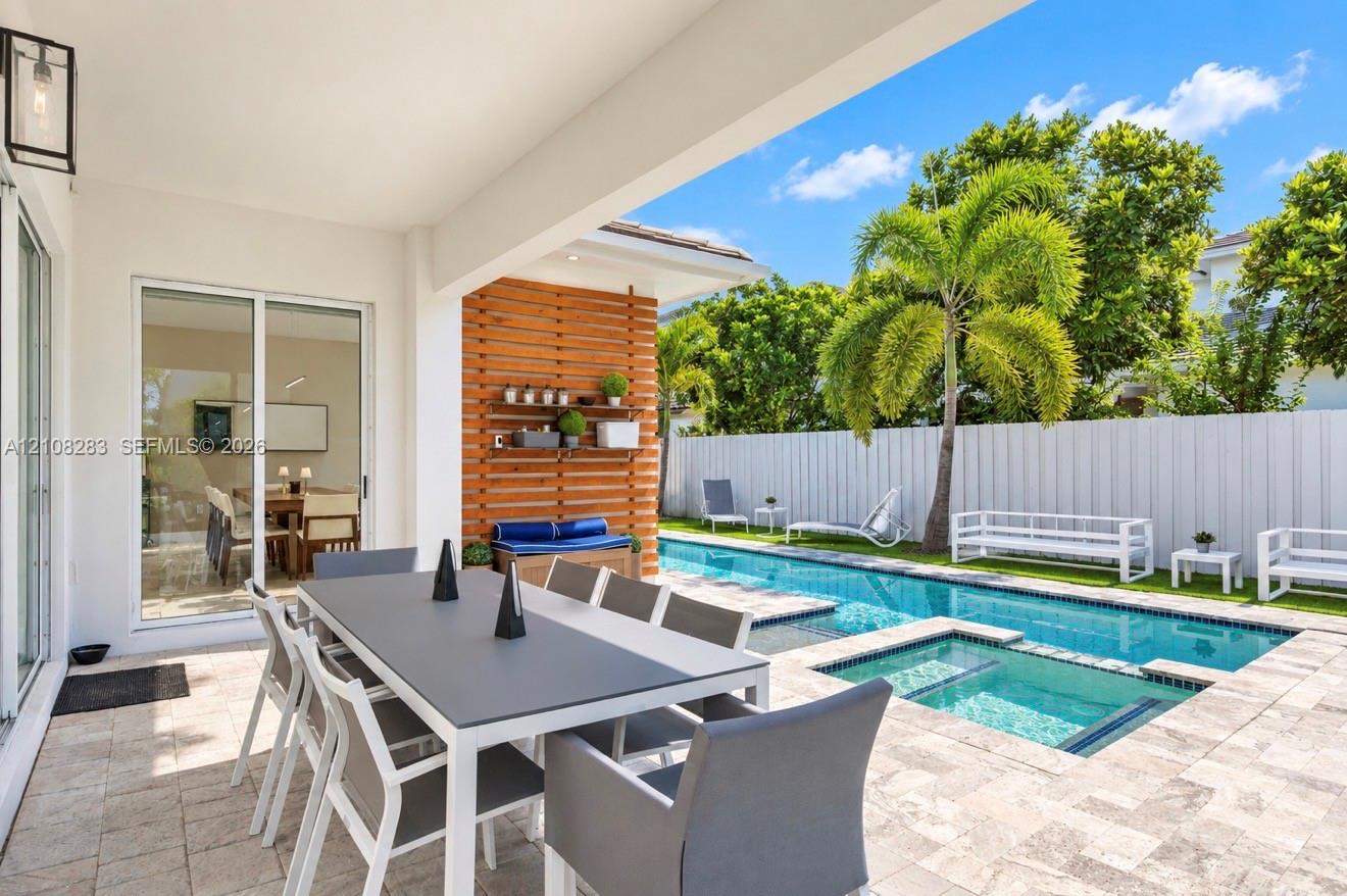 Covered patio featuring stone paver flooring, horizontal slat wood accent wall, built-in shelving, swimming pool with integrated spa, and vertical privacy fencing