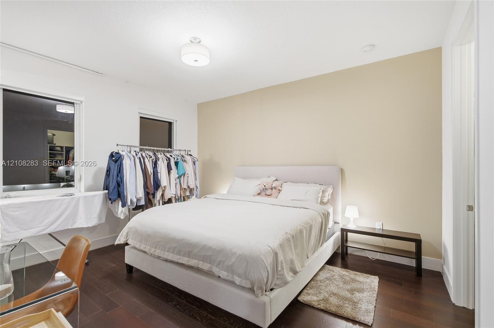 Bedroom featuring wood-finish flooring, two windows, a neutral accent wall, and a central ceiling-mounted light fixture