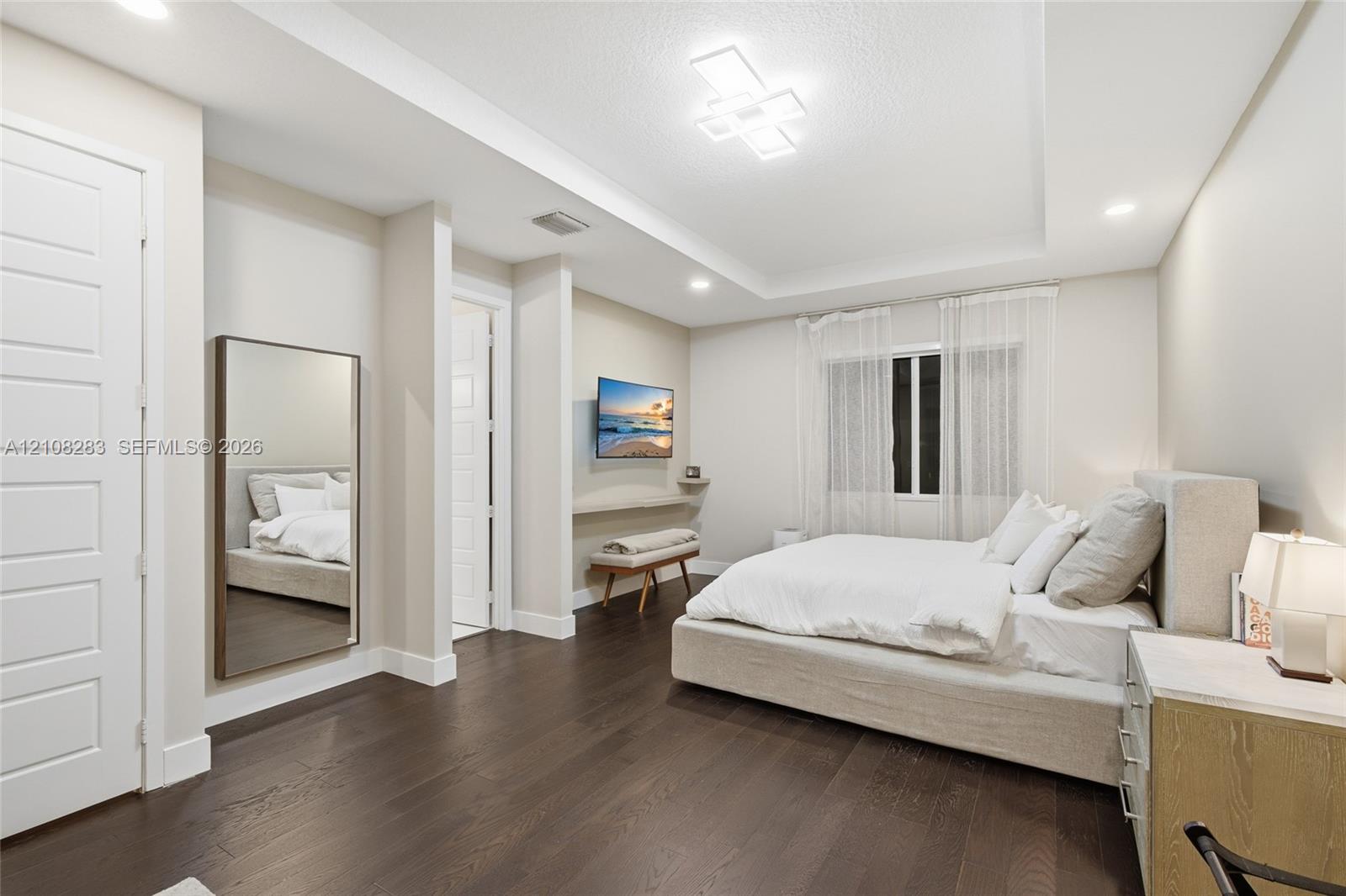 Bedroom featuring wood-finish flooring, tray ceiling with recessed and geometric modern lighting, and a wall-mounted floating display ledge