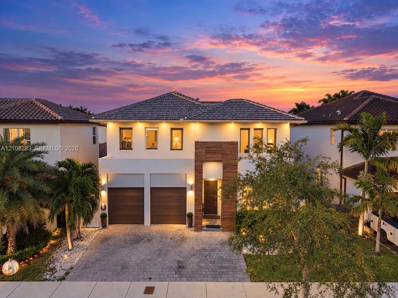 Two-story residence featuring a paved driveway, dual-car garage with wood-finish doors, contemporary tile roof, and textured stone facade accents