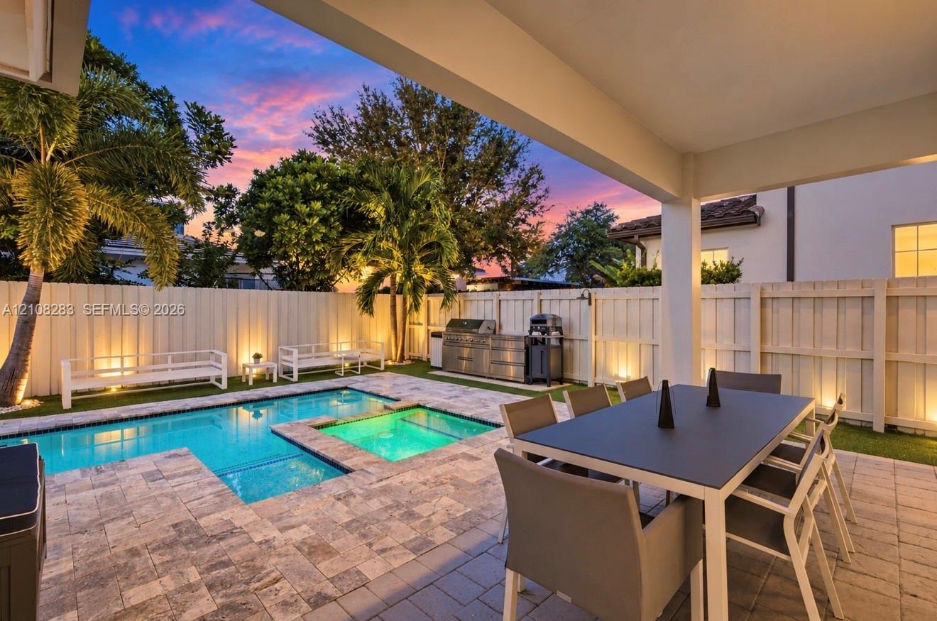 Covered patio featuring stone-paver decking, integrated swimming pool with inset spa, built-in stainless steel outdoor kitchen, and perimeter privacy fencing