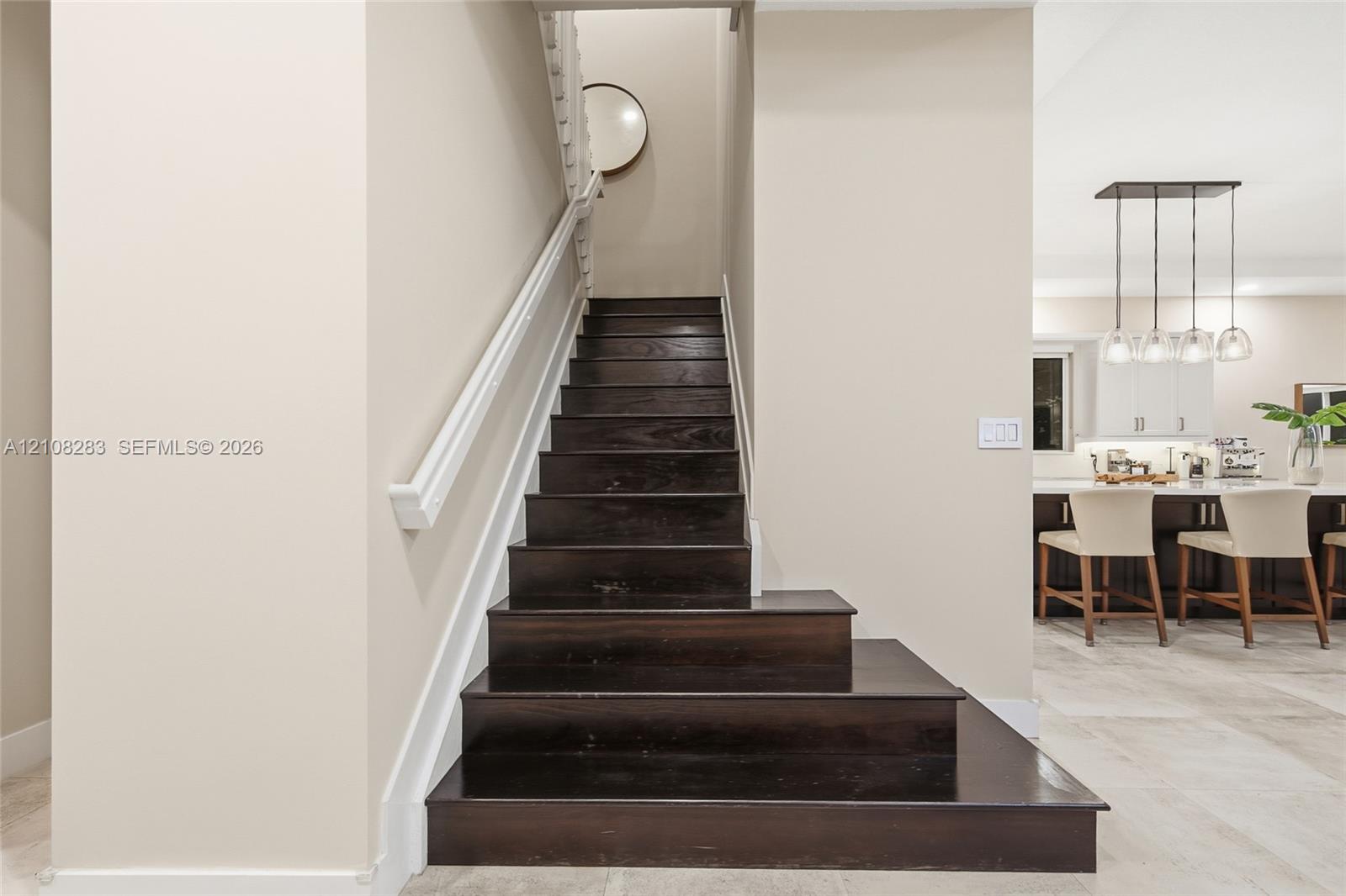 Staircase featuring dark wood-finish treads, white handrail, and white balusters, situated on stone-finish flooring with a multi-pendant light fixture and built-in cabinetry in the background