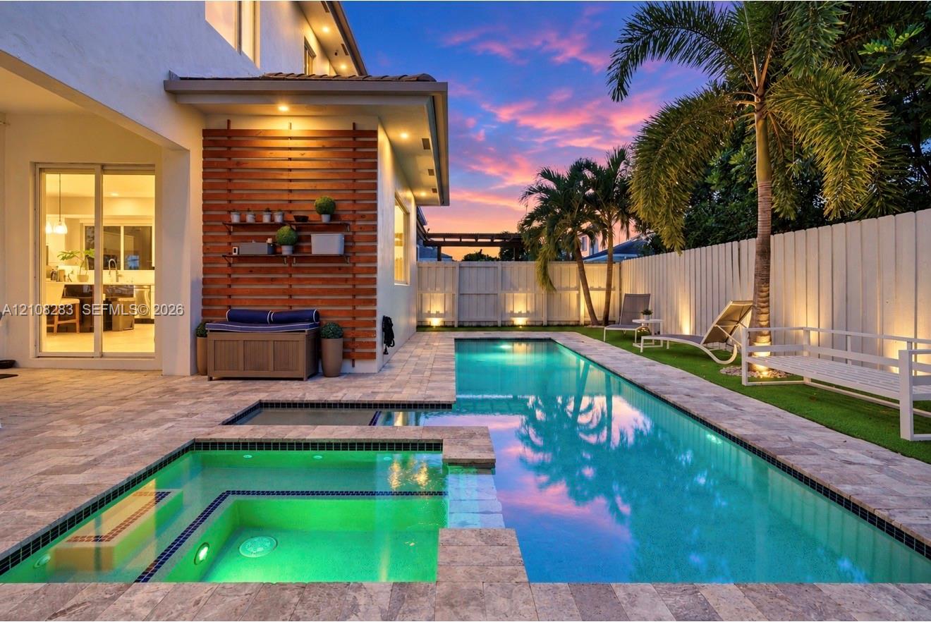 Outdoor living area featuring a rectangular swimming pool with an integrated spa, stone paver decking, horizontal wood-slat accent wall, and perimeter privacy fencing