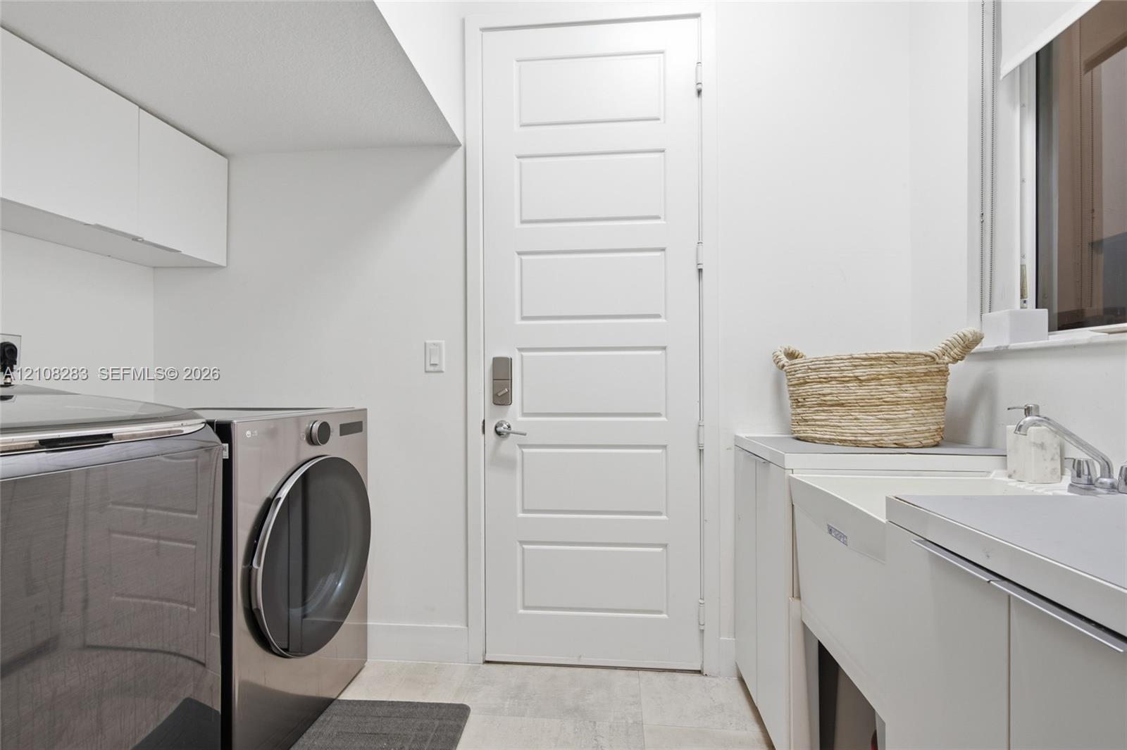 Laundry area featuring white cabinetry, a utility sink with a faucet, five-panel door, and tiled flooring