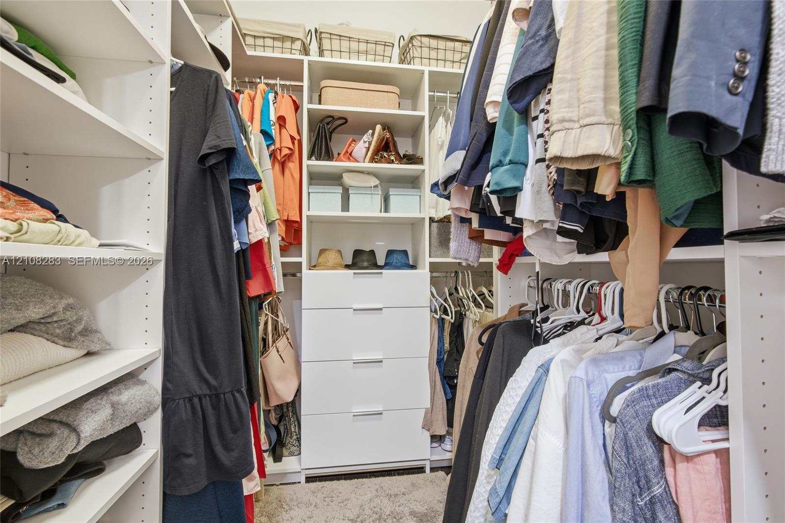 Walk-in closet featuring white custom built-in shelving, a central column of four soft-close drawers with metallic pulls, and multi-level hanging rods