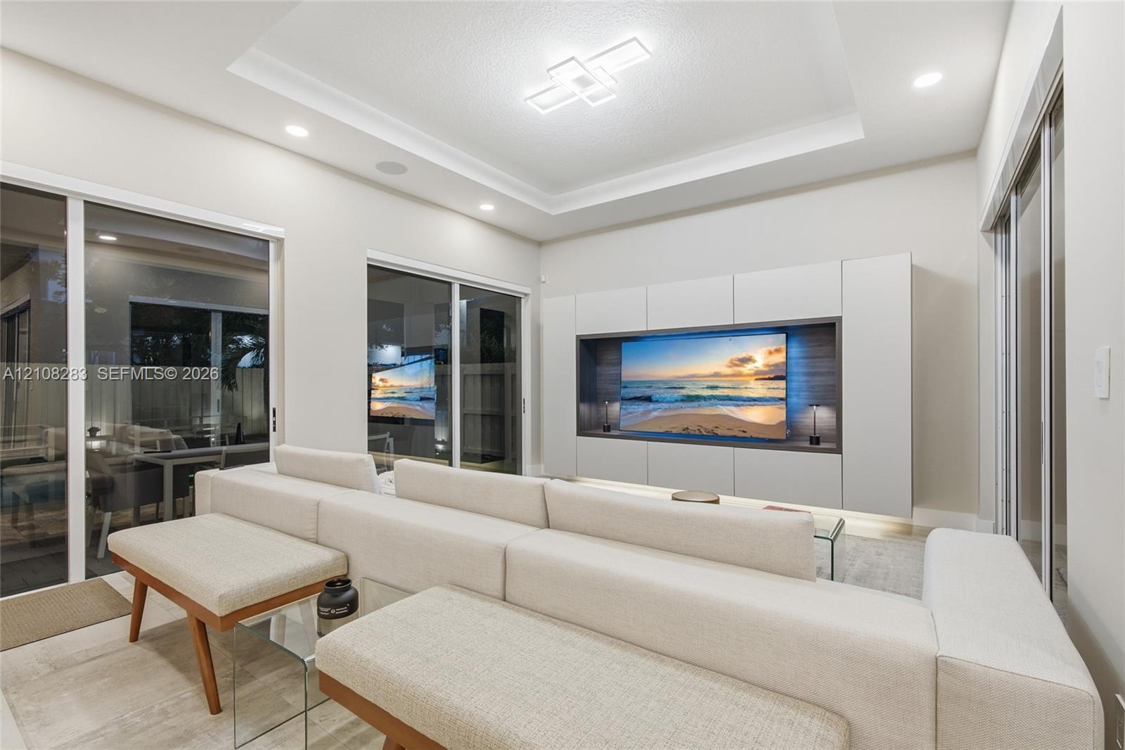 Tray ceiling with integrated geometric lighting, large-format tile flooring, and custom built-in cabinetry featuring recessed media display with wood-toned back paneling and under-cabinet illumination