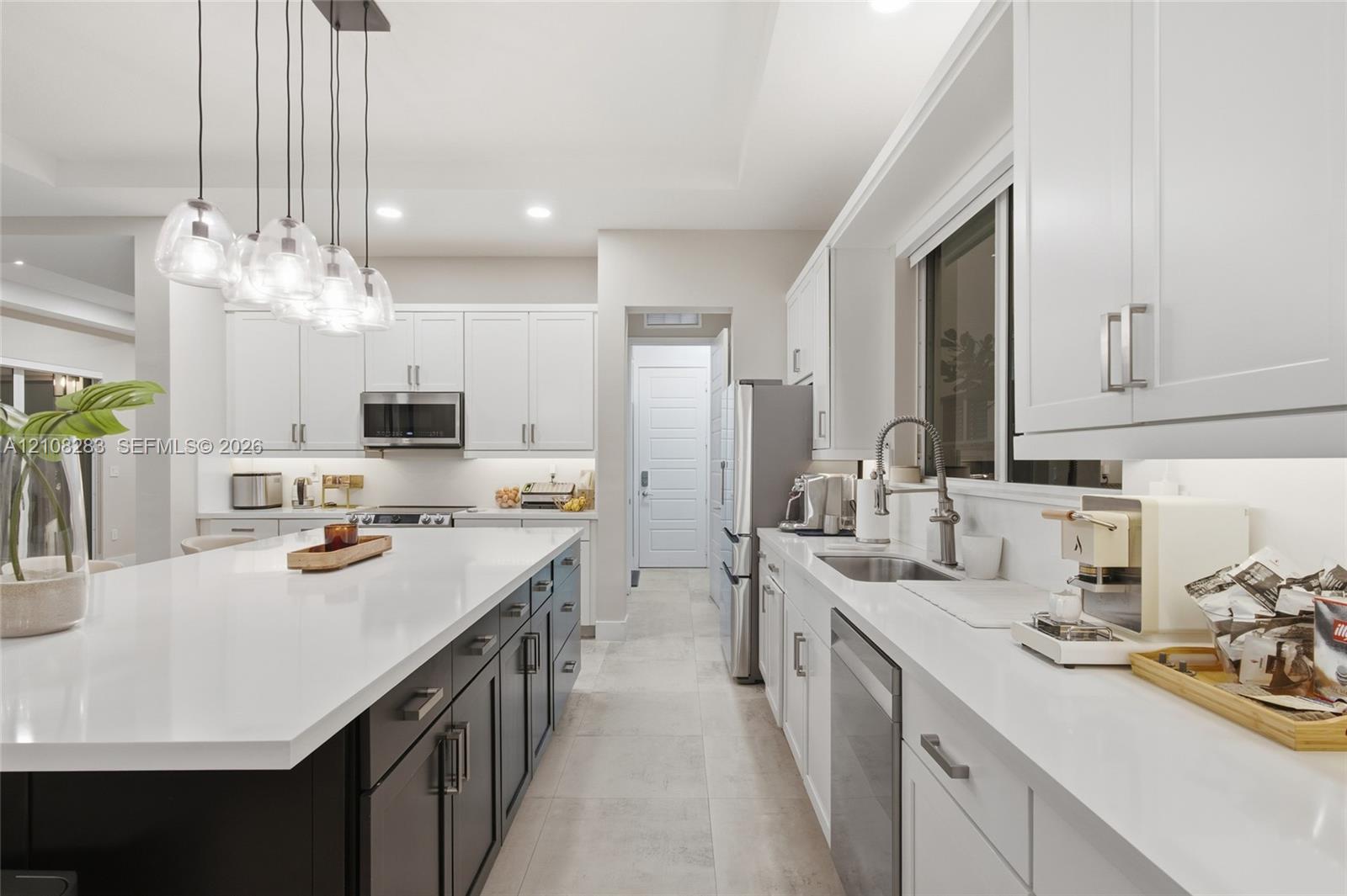 Kitchen featuring a central island with a solid-surface countertop, white shaker-style cabinetry, stainless steel appliances, and multi-light pendant fixture