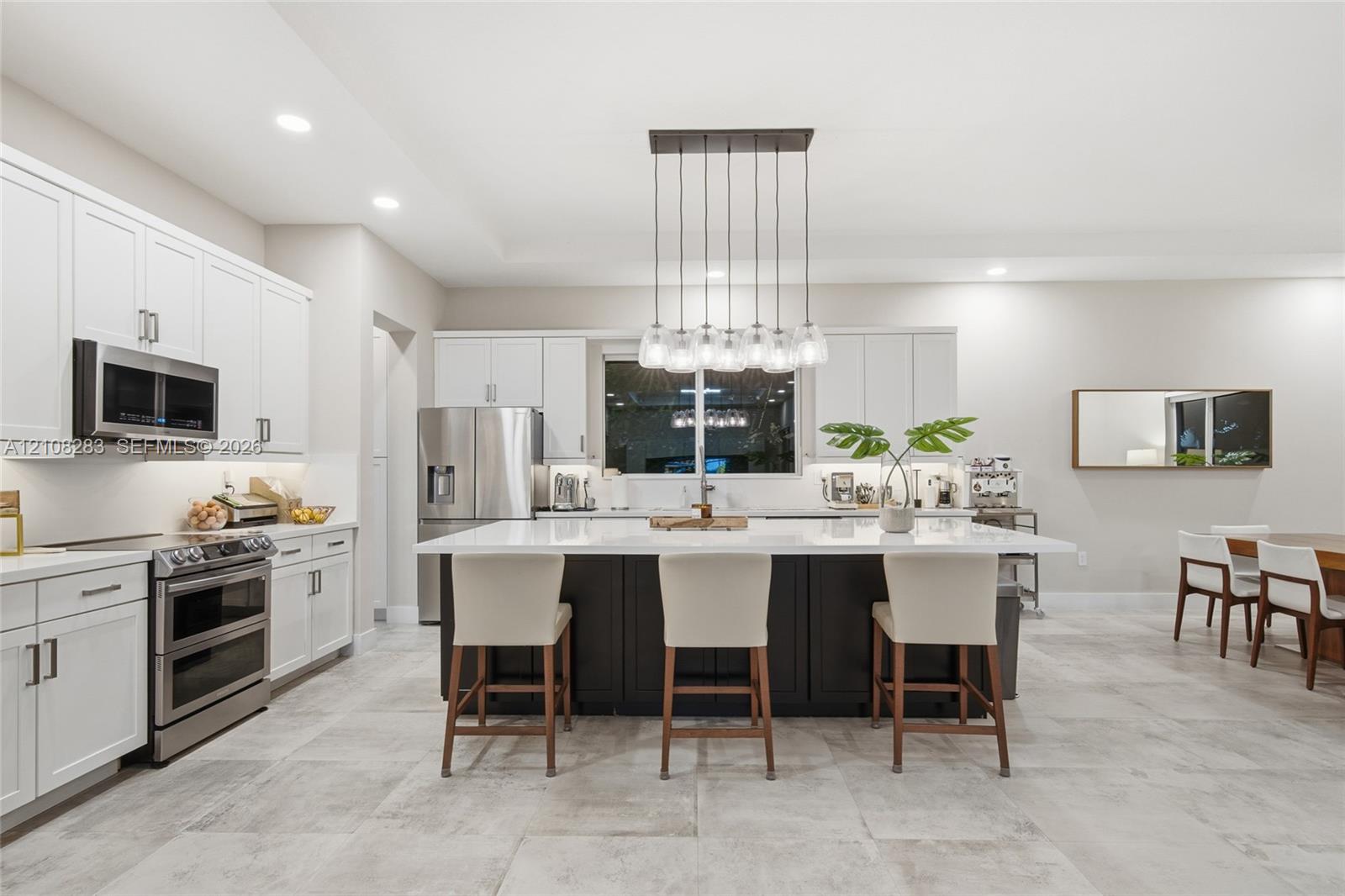 Kitchen featuring white shaker-style cabinetry, a contrasting dark-toned kitchen island with a light-toned solid surface countertop, stainless steel appliances, and tile flooring