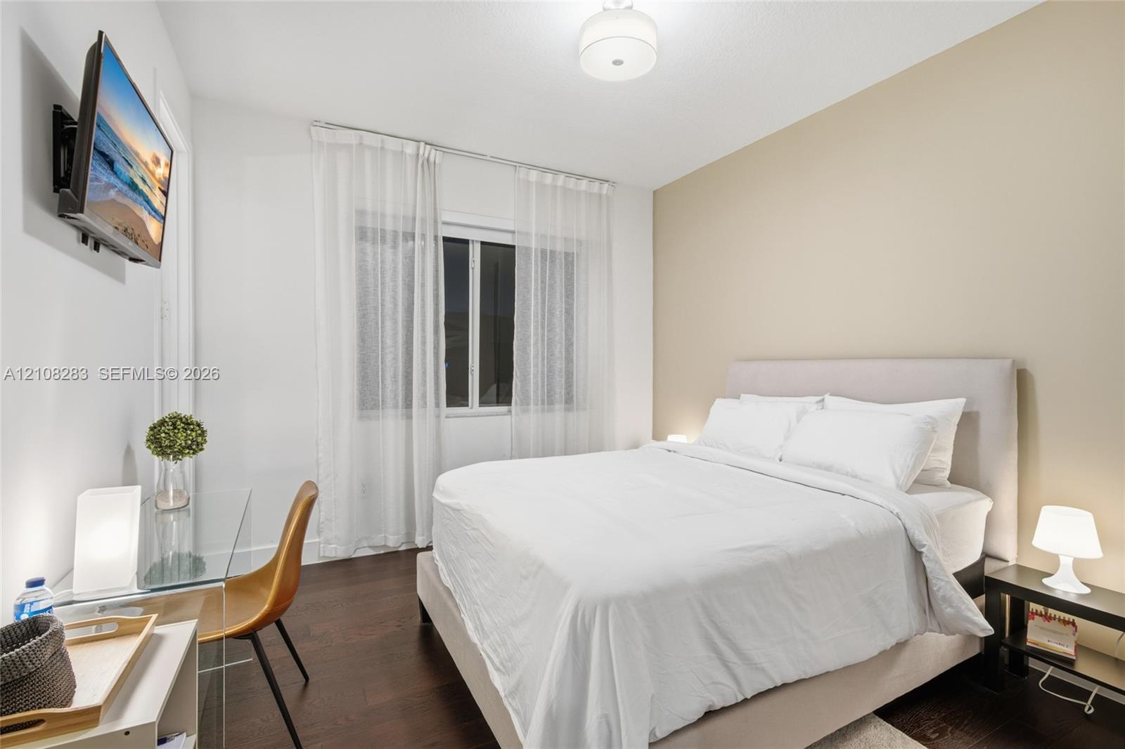 Room featuring dark wood-finish flooring, neutral-toned accent wall, and a central ceiling-mounted drum light fixture