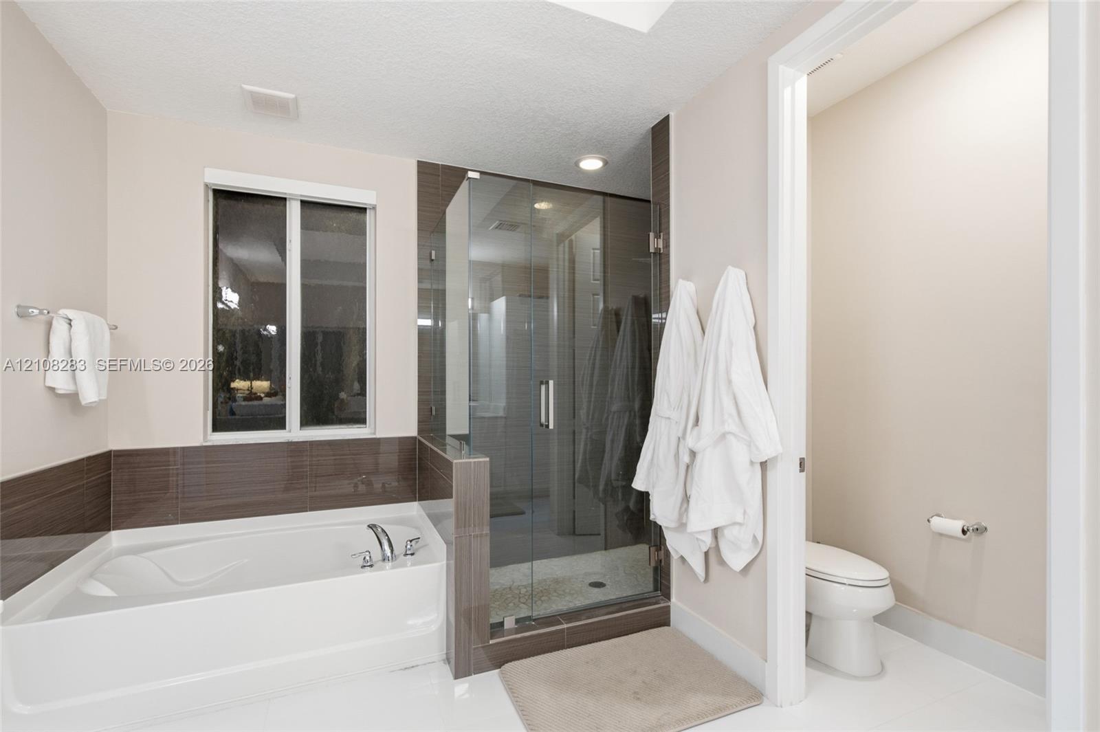 Built-in soaking tub with a tiled surround, glass-enclosed shower, polished finish flooring, and wall-mounted metal fixtures