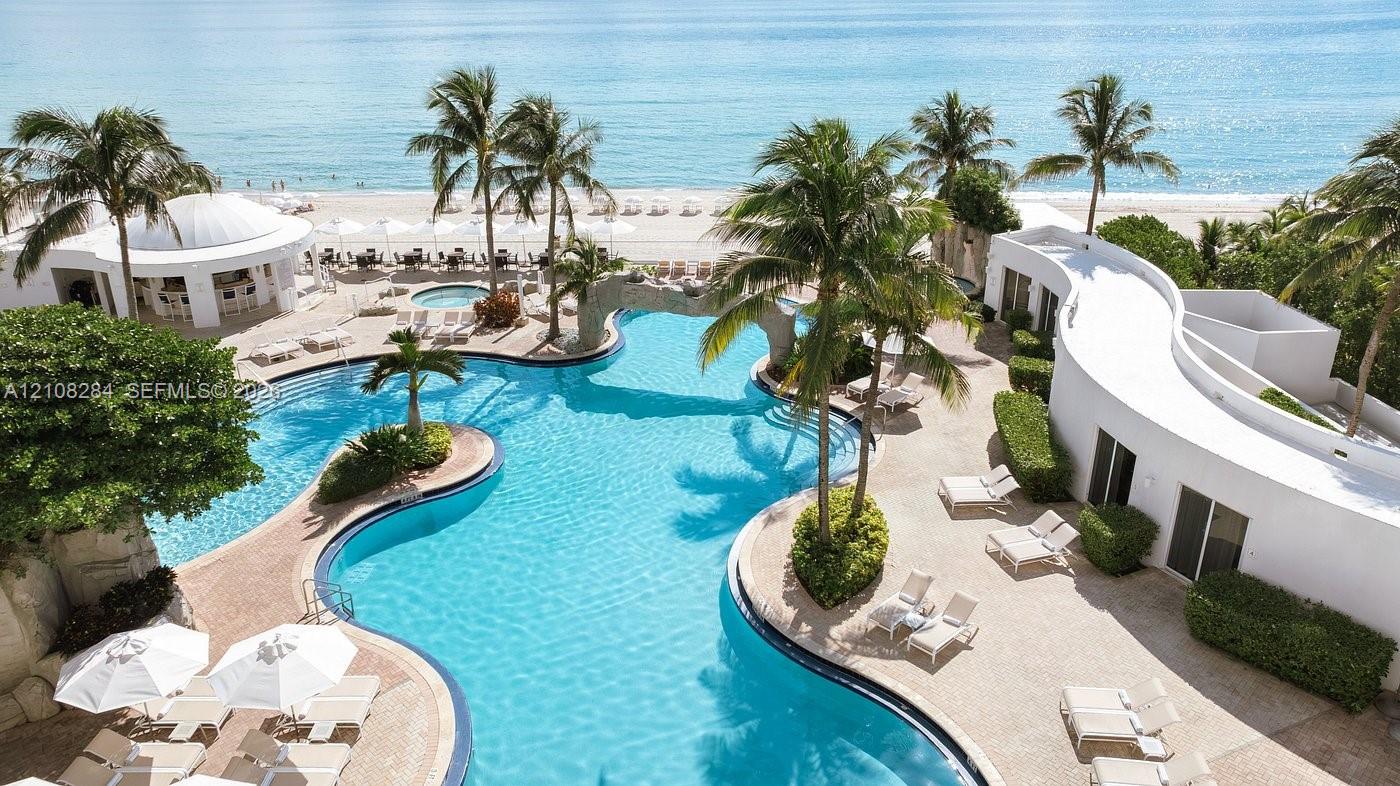 Freeform swimming pool with integrated rock features, surrounding paved deck, palm tree landscaping, and direct beach access