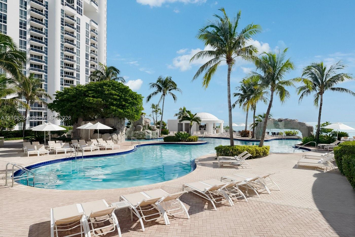 Resort-style swimming pool featuring rock waterfall features, paver decking, and integrated landscaping