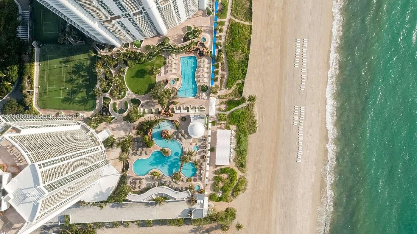 Aerial perspective featuring direct beach access, multiple outdoor swimming pools, a tennis court, and manicured grounds