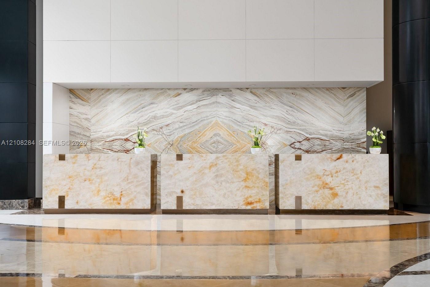 Reception desk featuring stone paneling with book-matched detailing, polished natural stone flooring, and contrasting matte black architectural columns