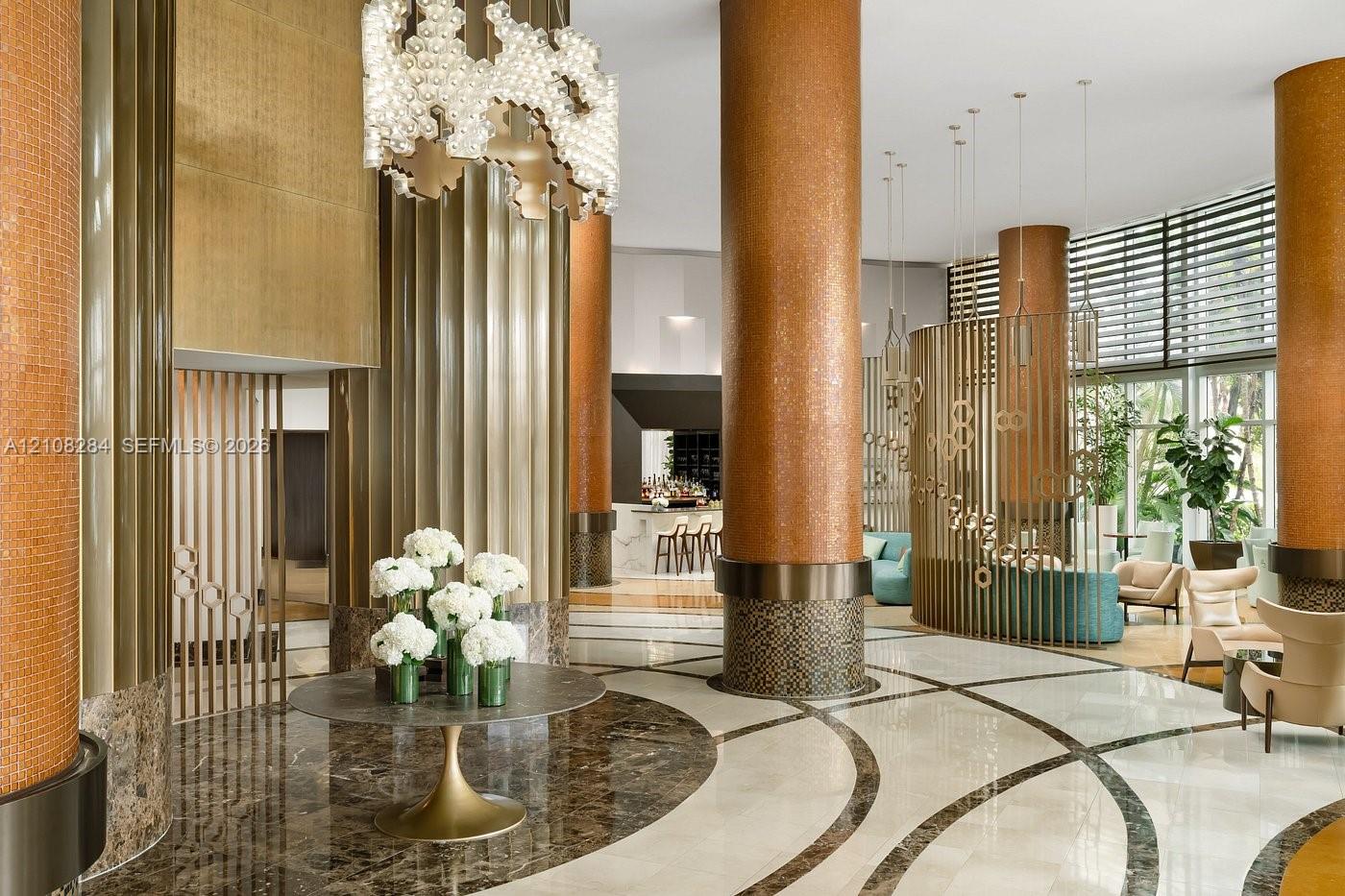 Grand lobby featuring polished stone flooring with inlaid patterns, metallic-finished structural columns, decorative vertical screening, and tiered custom chandelier lighting