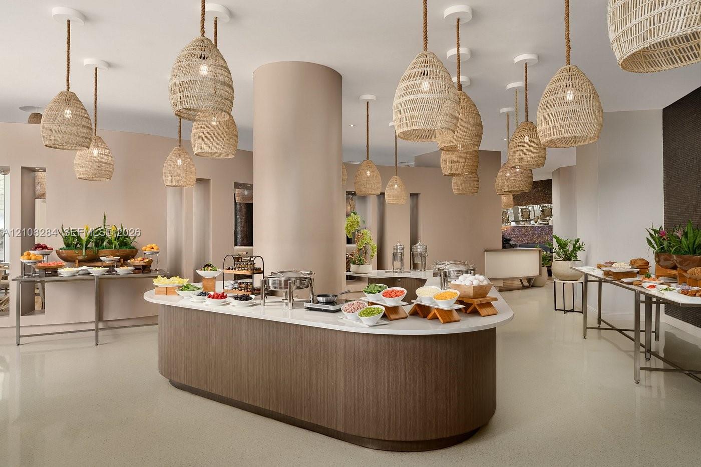 Curved central island featuring a light-toned countertop and wood-finish cabinetry, illuminated by an array of woven pendant lighting, complemented by polished flooring