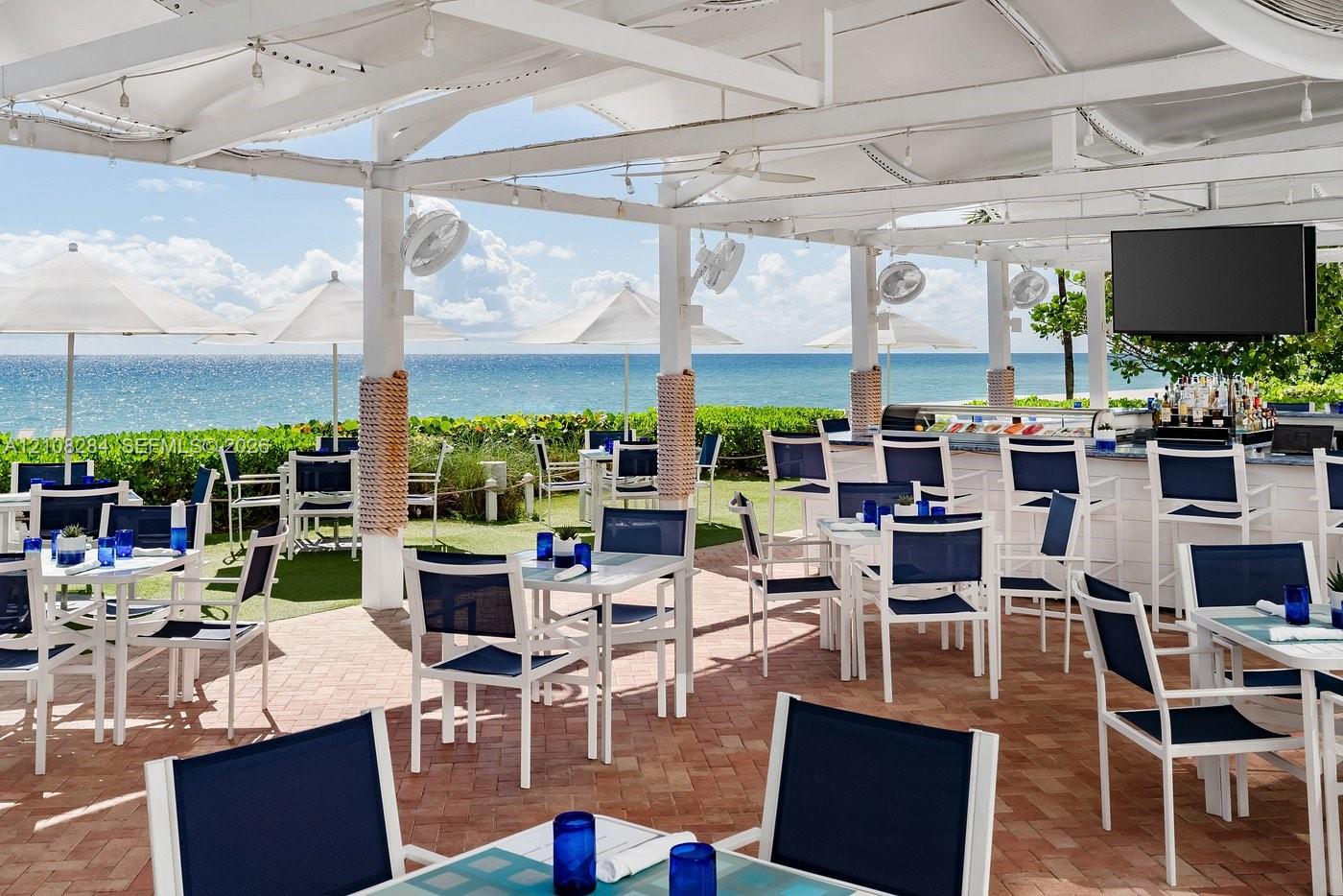 Covered outdoor terrace featuring a white pergola structure, brick pavers, wall-mounted ceiling fans, and an integrated bar counter