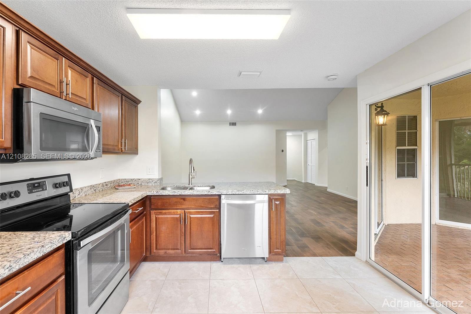Kitchen featuring wood cabinetry, stone-finish countertops, stainless steel appliances, tile flooring, and sliding glass doors