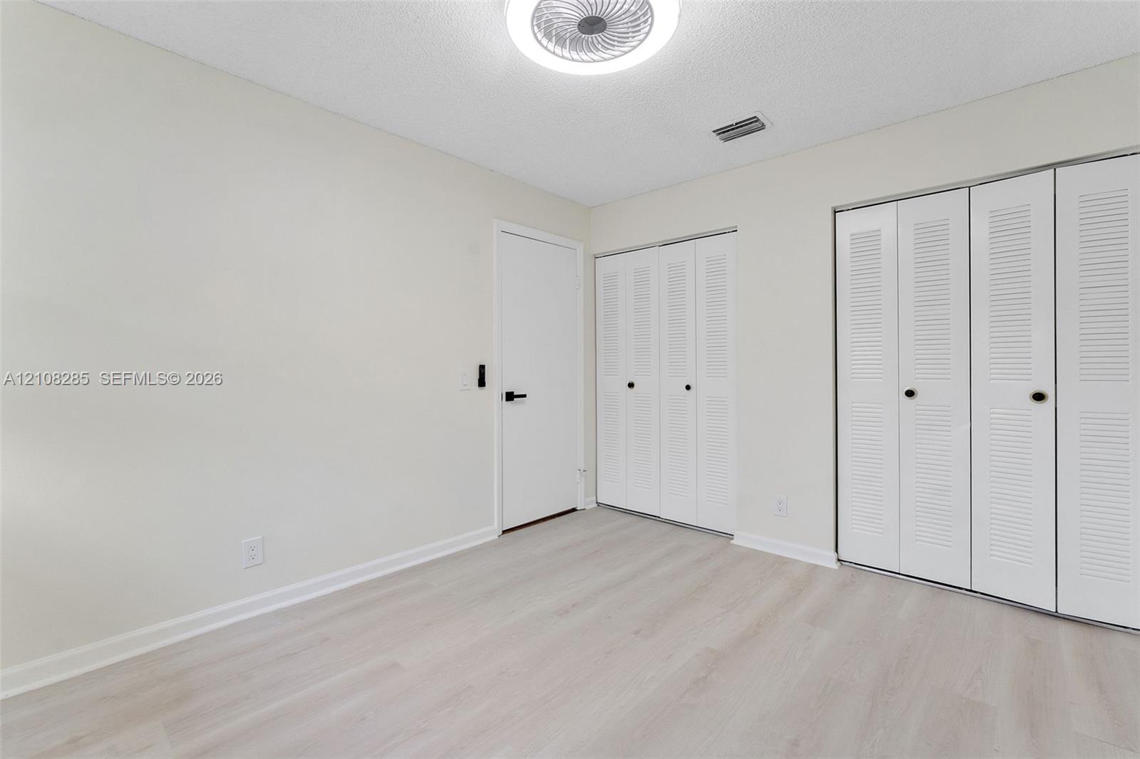 Neutral-toned room featuring wood-finish flooring, dual closets with louvered doors, and a central circular flush-mount ceiling light