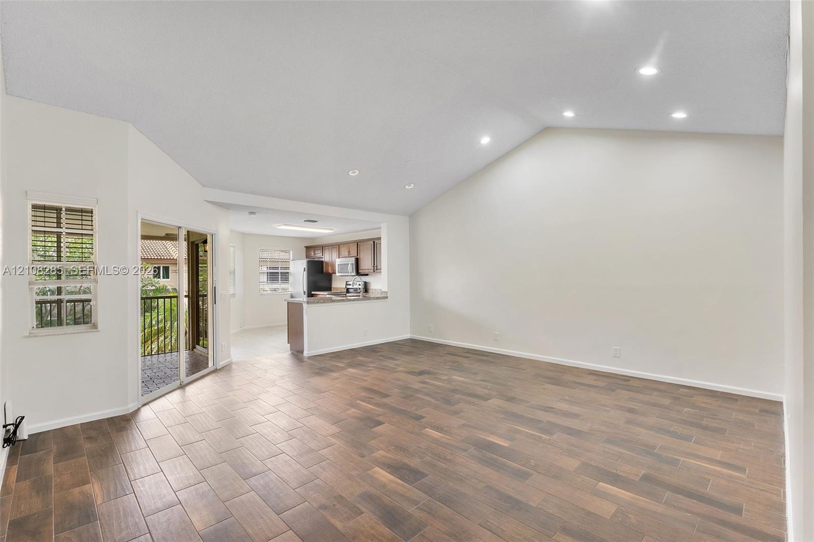 Vaulted ceilings with recessed lighting, wood-finish tile flooring, and glass sliding doors