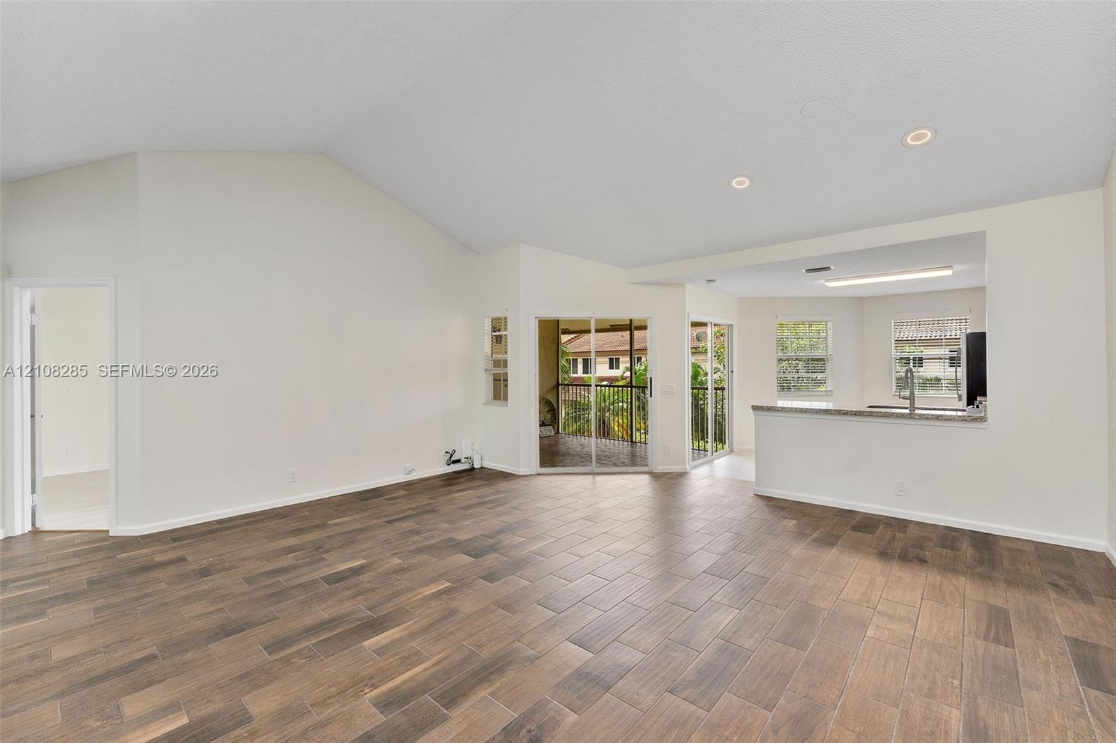 Vaulted ceilings, wood-finish tile flooring, recessed lighting, and sliding glass doors with access to a balcony