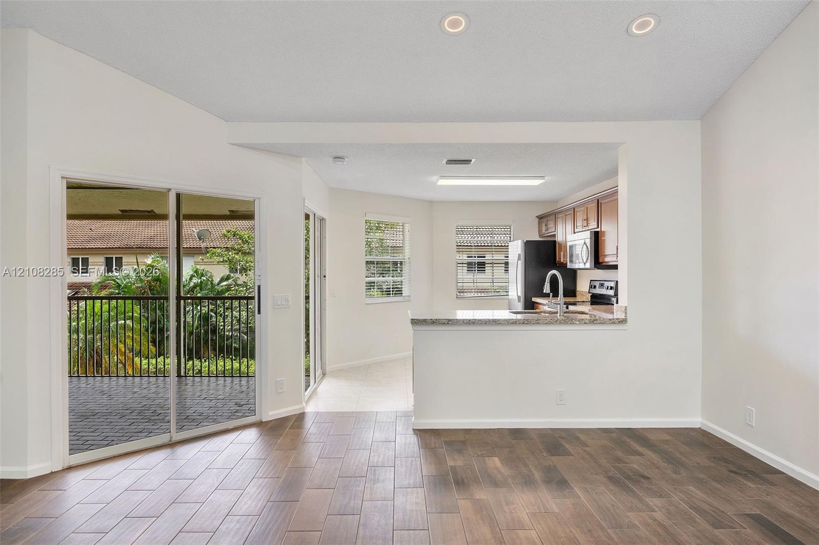 Open-concept space featuring wood-finish flooring, recessed lighting, a kitchen pass-through with a stone-finish countertop, and sliding glass doors with exterior balcony access