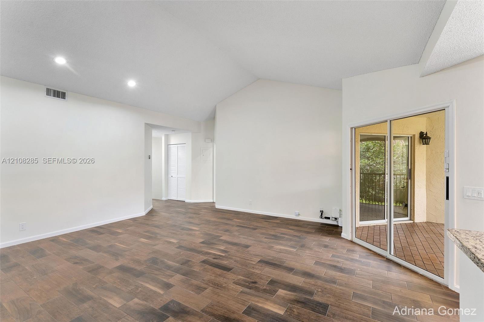 Interior space featuring vaulted ceilings, recessed lighting, and wood-finish flooring, with a glass sliding door providing access to a covered outdoor balcony