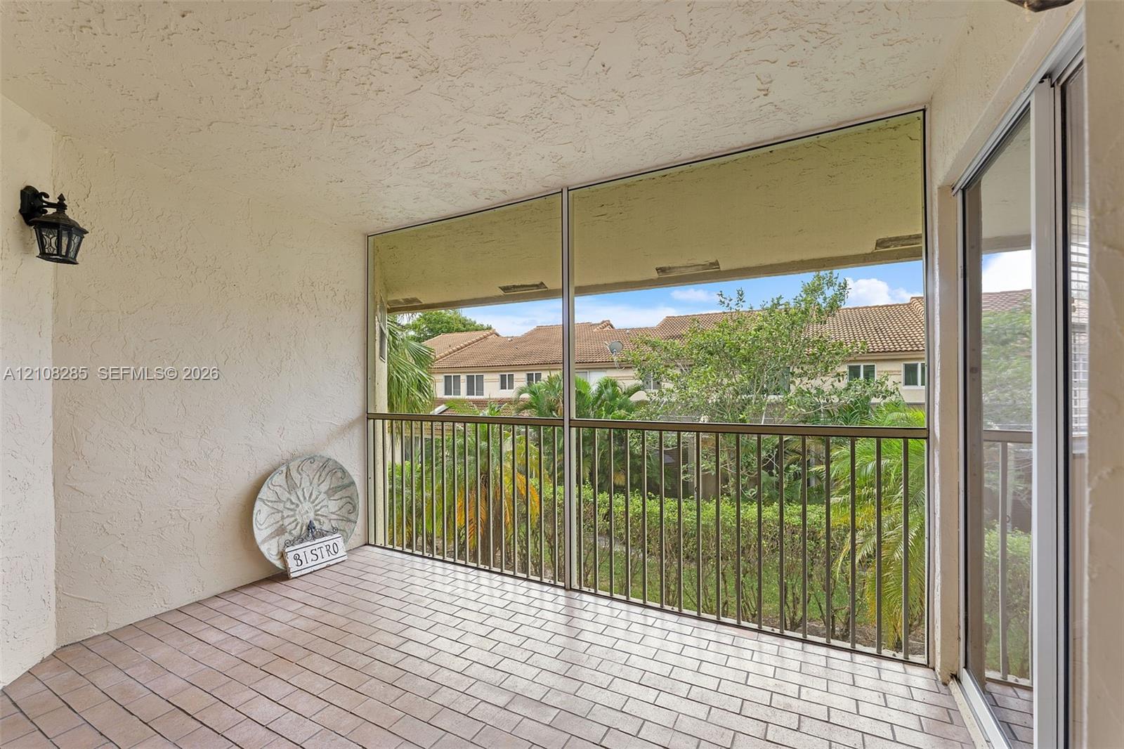 Covered balcony featuring tile flooring, metal railings, a screened enclosure, and wall-mounted exterior lighting
