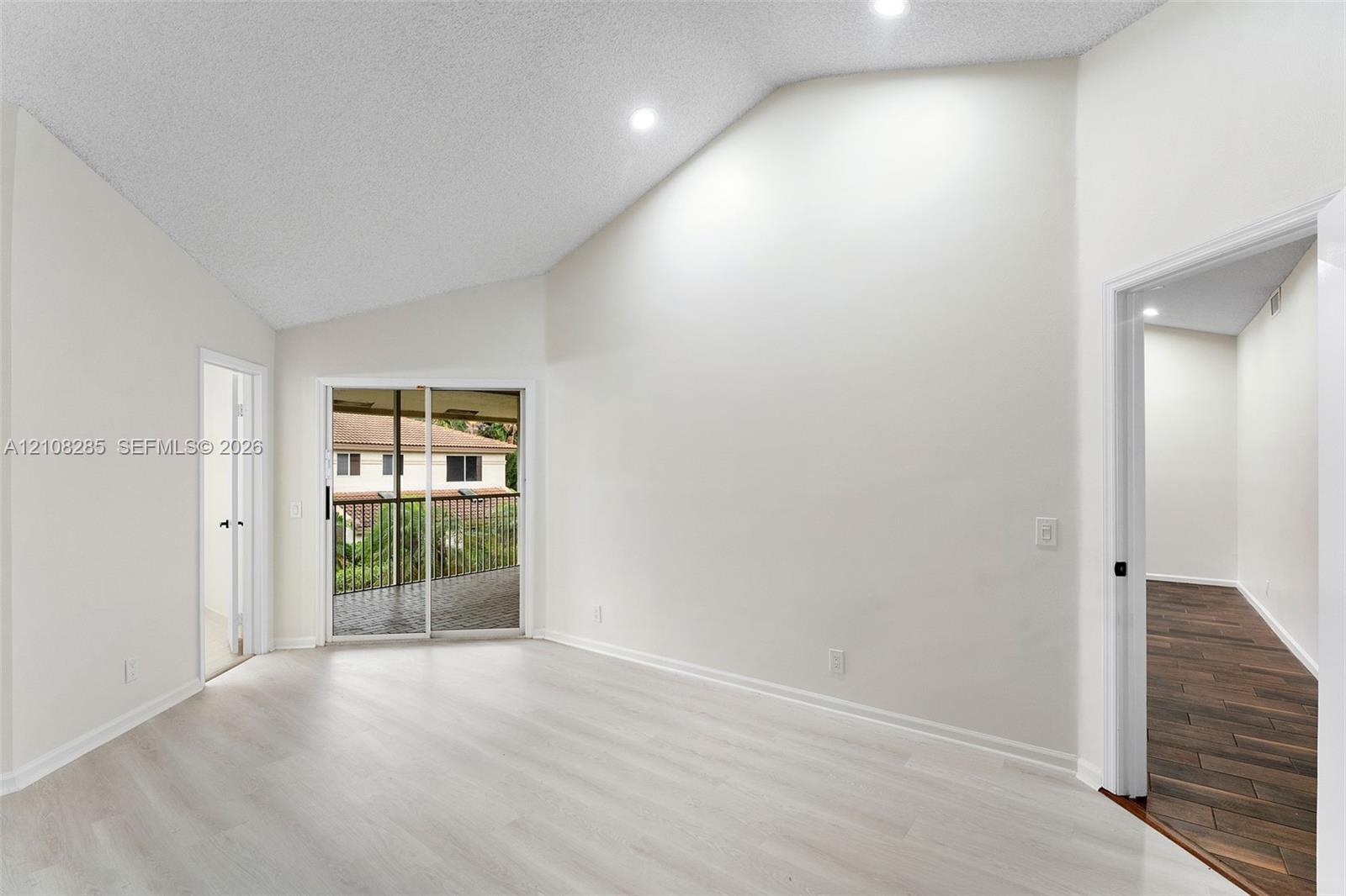 Vaulted ceilings featuring recessed lighting, light-toned wood-finish flooring, and sliding glass doors to a covered balcony