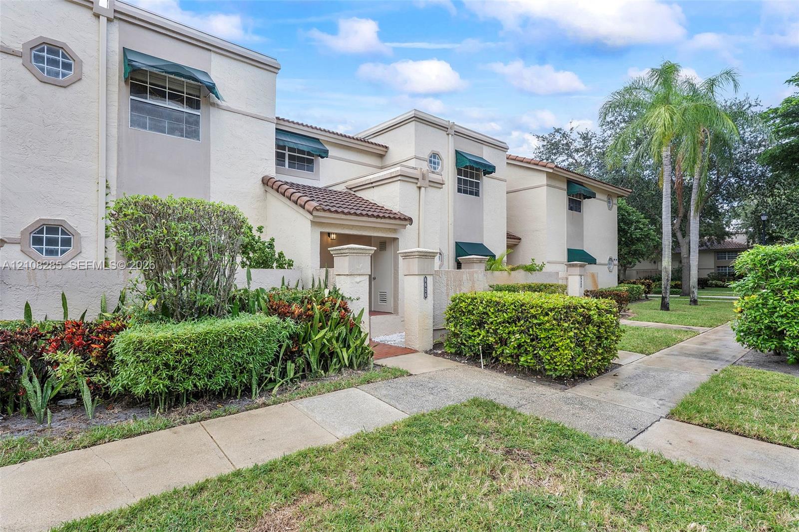 Multi-story stucco exterior featuring tile roofing, green window awnings, octagonal accent windows, and a paved walkway entry