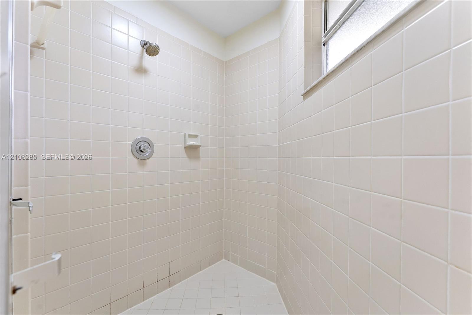 Shower stall featuring floor-to-ceiling square tile, a built-in soap niche, an integrated window, and a wall-mounted shower head with single-handle control