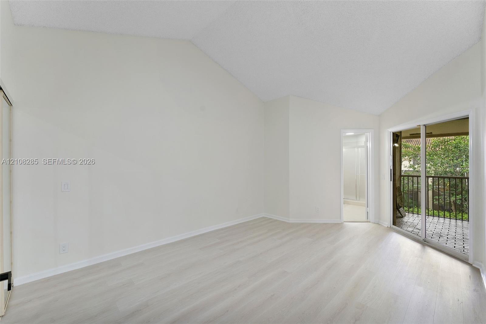 Vaulted ceilings, wood-finish flooring, and sliding glass doors with exterior balcony access