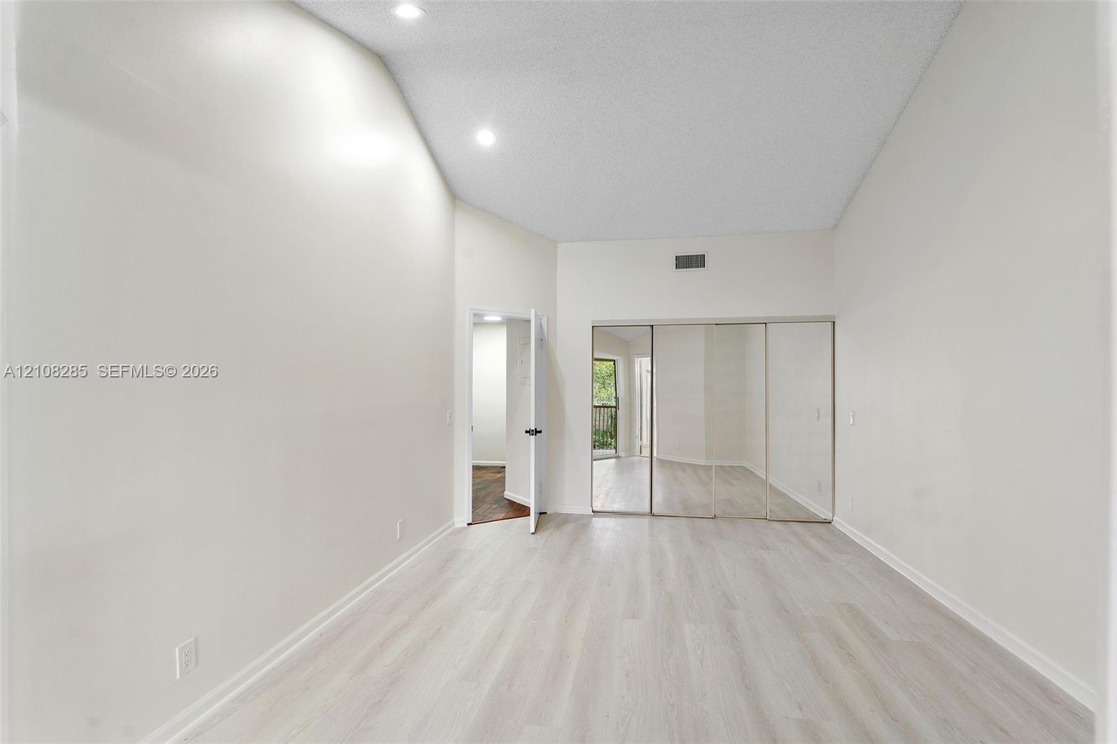 Vaulted ceilings featuring recessed lighting, light-toned wood-finish flooring, and mirrored closet doors