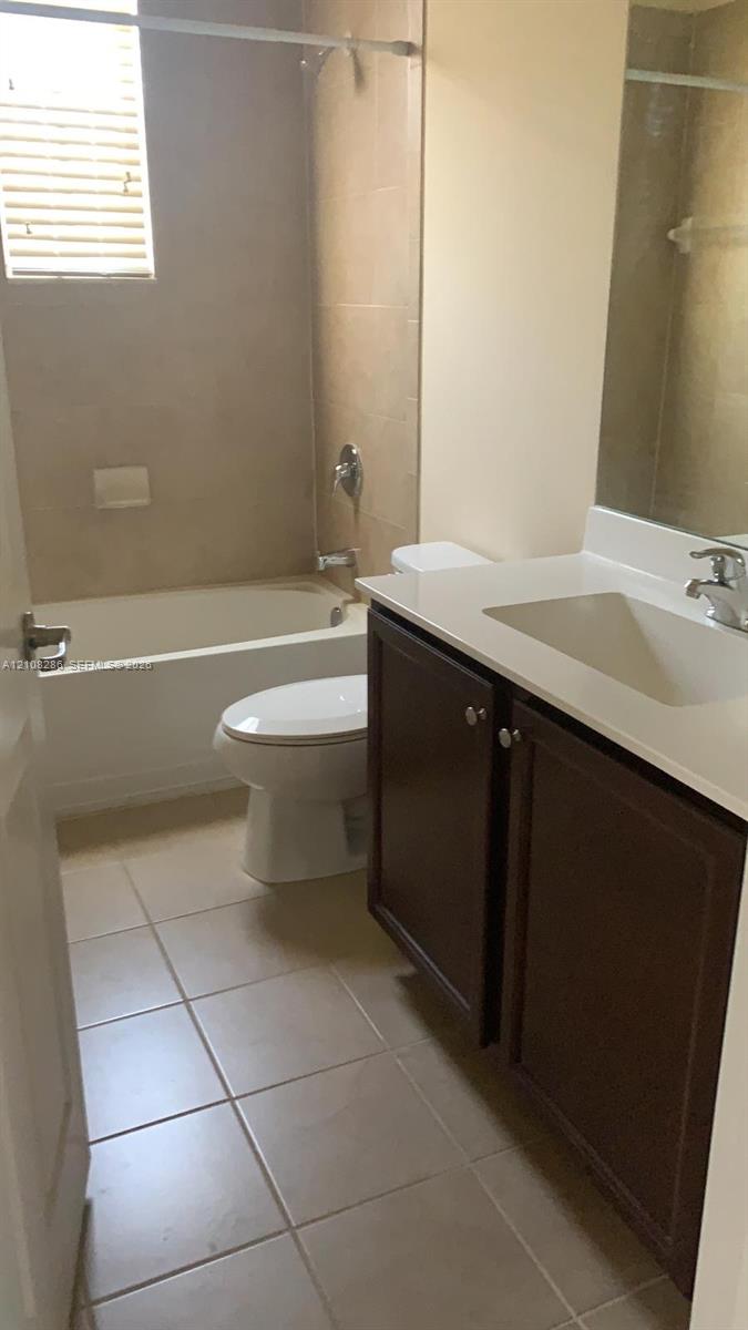 Bathroom featuring a vanity with dark-finish cabinetry, a light-toned countertop with an integrated basin, tile flooring, and a tiled shower-tub combination