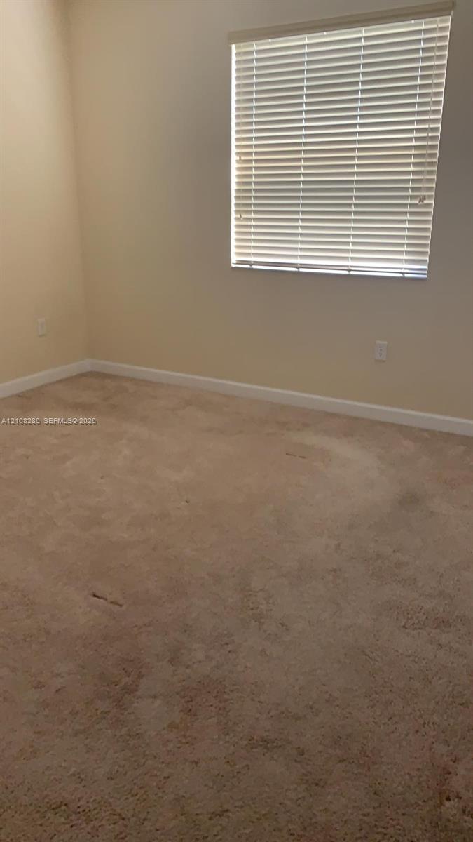 Neutral-toned interior space featuring carpeting and a window equipped with horizontal blinds
