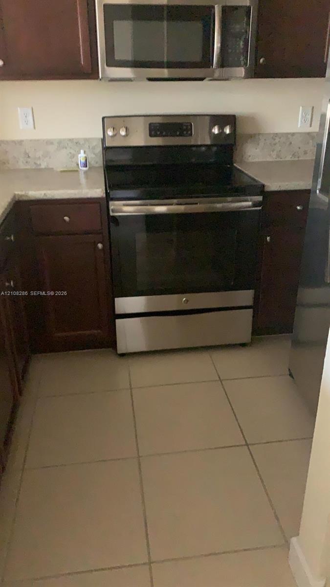 Kitchen featuring dark-finish cabinetry, neutral-toned countertops, tile flooring, and stainless steel appliances including an electric range and built-in microwave