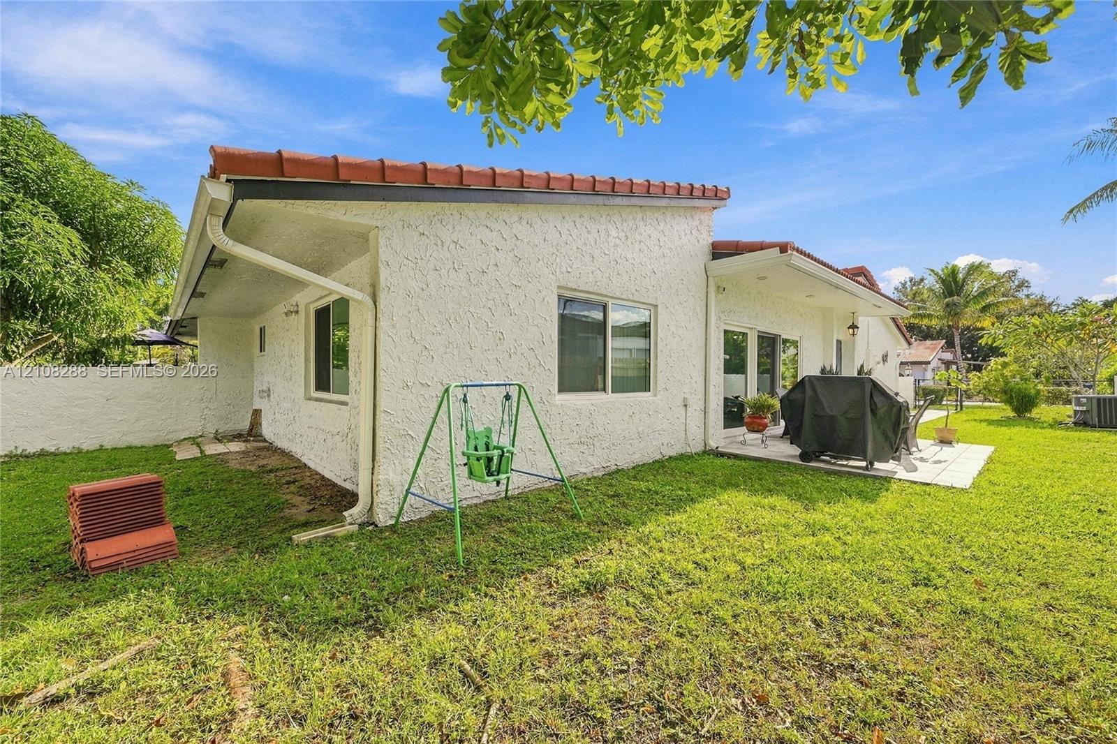 Exterior featuring stucco siding, a low-slope roof with clay tiles, a concrete patio, and an expansive lawn