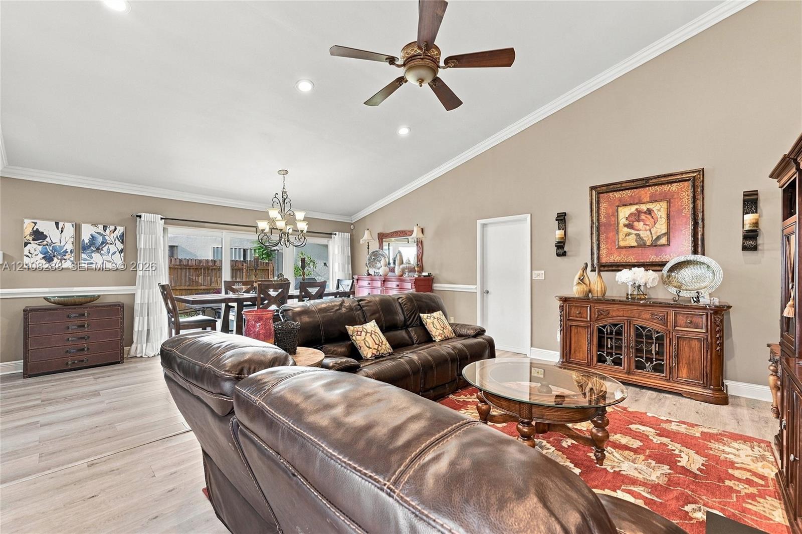 Living area featuring a vaulted ceiling, wood-finish flooring, crown molding, chair rail trim, and a ceiling fan Living area featuring a vaulted ceiling, wood-finish flooring, crown molding, chair rail trim, and a ceiling fan