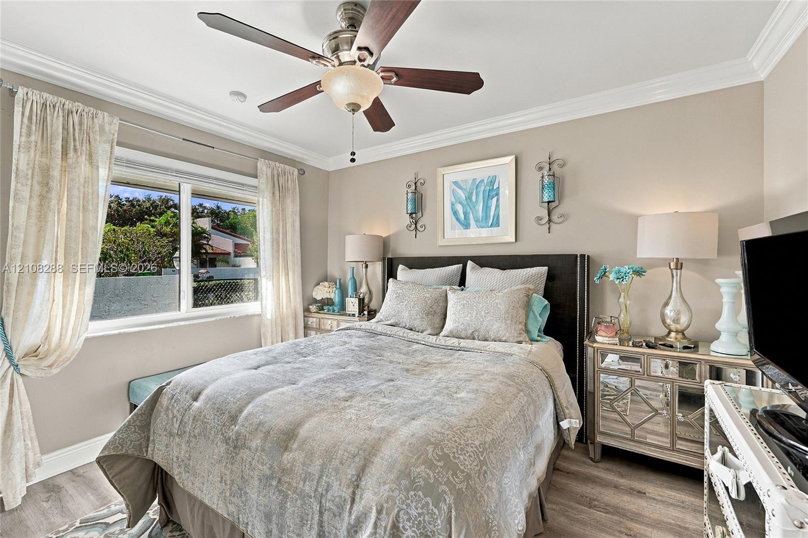 Neutral-toned 2nd bedroom featuring wood-finish flooring, crown molding, and a multi-blade ceiling fan with an integrated light fixture