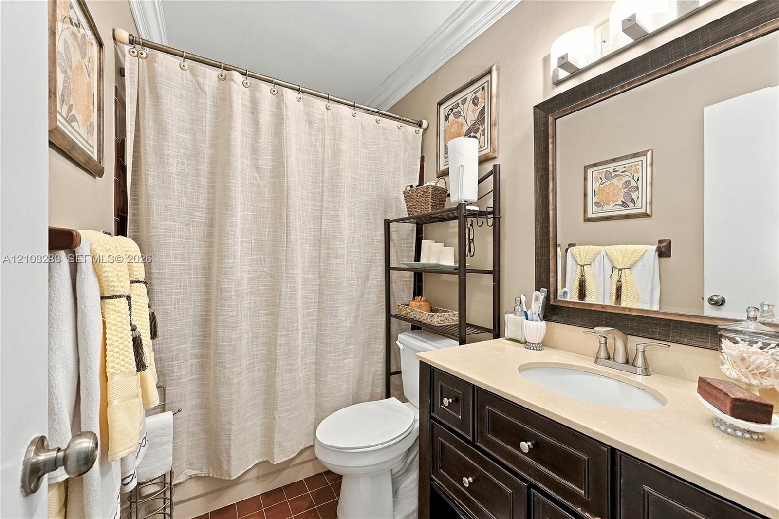 Guest Bathroom featuring a vanity with dark-finish cabinetry, a light-toned countertop, and an undermount oval sink, complemented by a framed wall mirror, crown molding, and tiled flooring