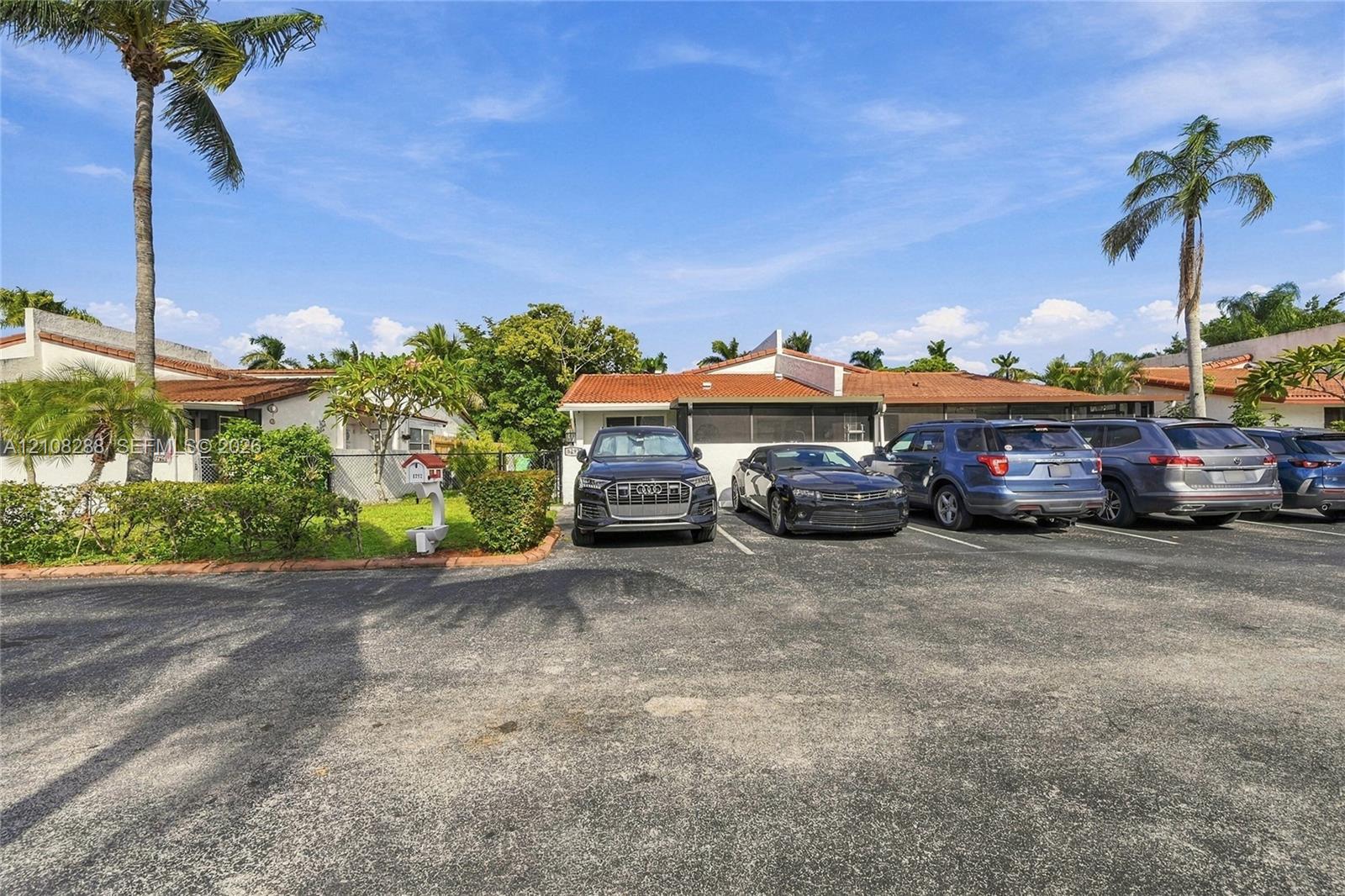 Single-story exterior featuring a clay tile roof, paved off-street parking, and established landscaping with mature palm trees Single-story exterior featuring a clay tile roof, paved off-street parking, and established landscaping with mature palm trees