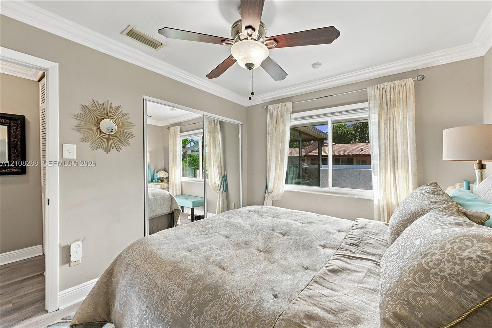 Neutral-toned interior featuring crown molding, a ceiling fan with integrated lighting, and mirrored sliding closet doors