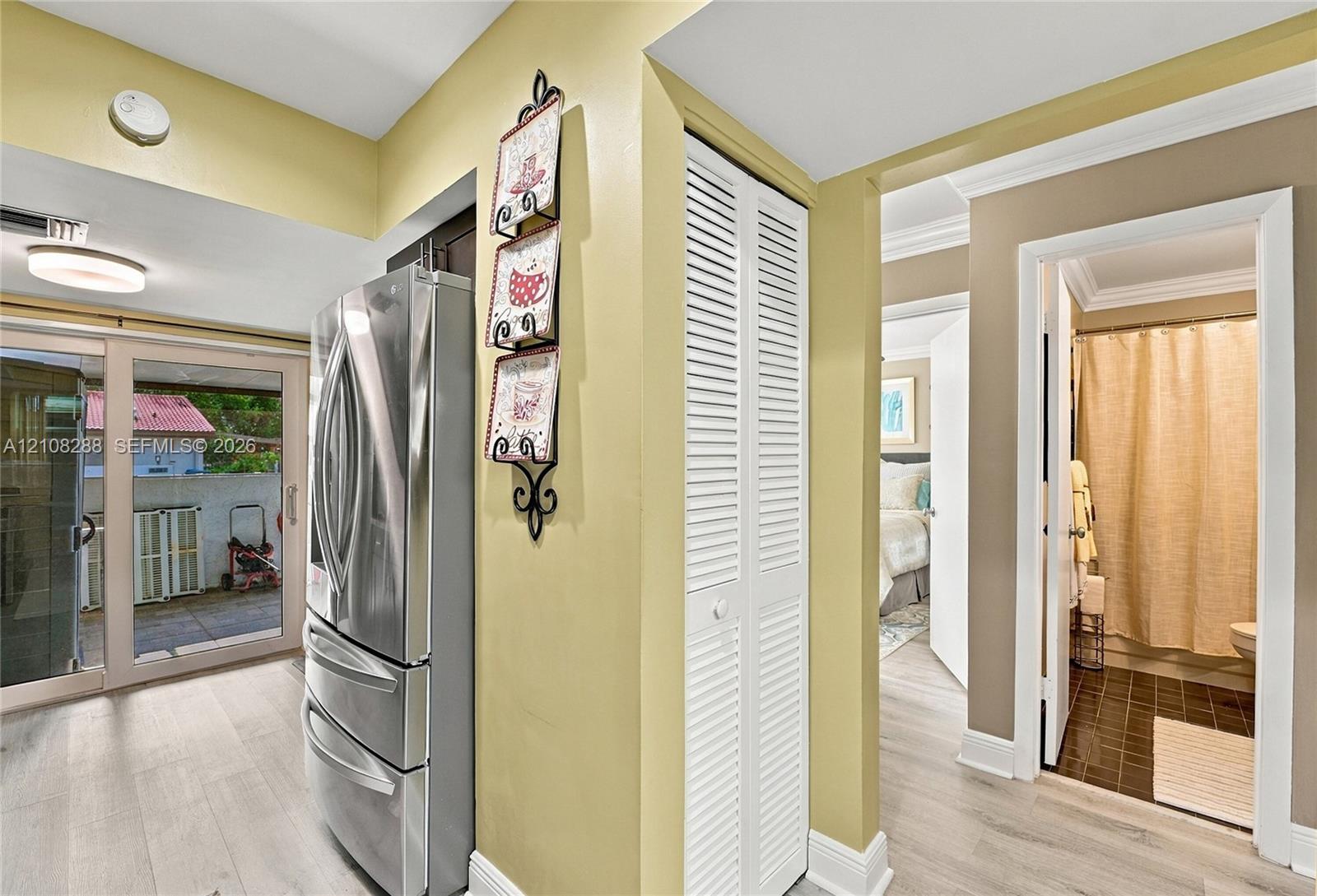 Stainless steel French door refrigerator, wood-finish flooring, white louvered-door closet, and glass sliding door featuring an exterior balcony