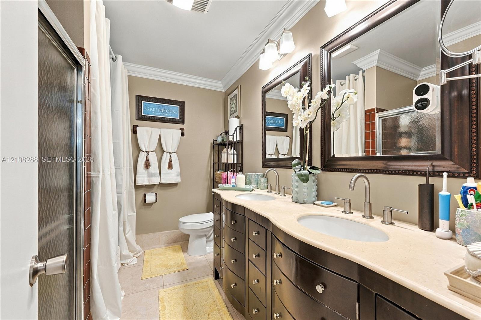 Dual-sink vanity with dark-finish cabinetry, stone countertop, two framed mirrors, and crown molding