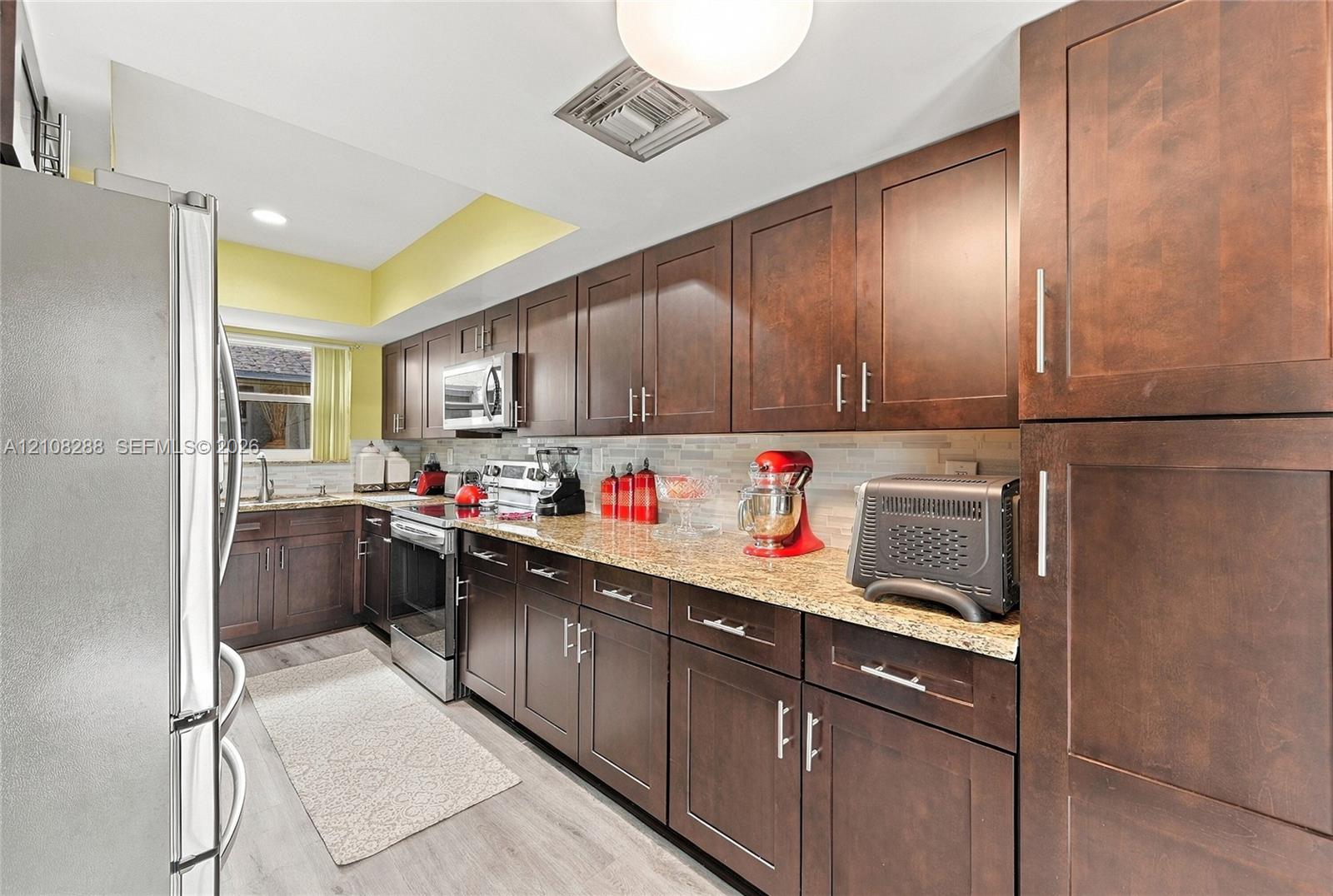 Kitchen featuring dark wood-finish cabinetry, stone-style countertops, stainless steel appliances, and a light-toned tile backsplash